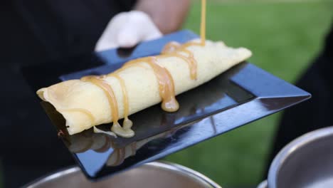 chef drizzling hot caramel syrup sauce on crepe, outdoor venue food service