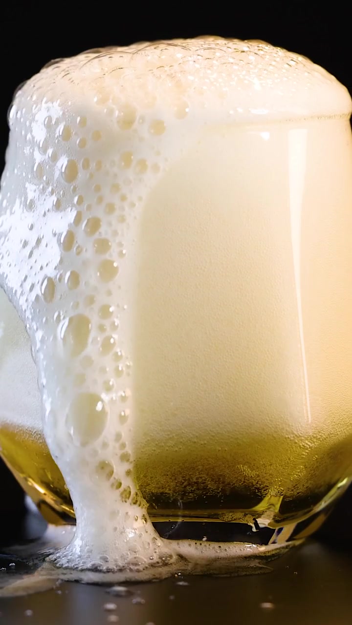 Un'inquadratura verticale che mostra birra dorata riempire un bicchiere fino a quando una spessa schiuma bianca non trabocca.