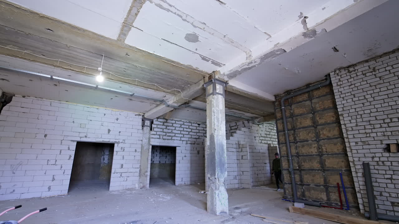 Man enters the large premise of the construction. Light bulb switched on hangs on the ceiling.