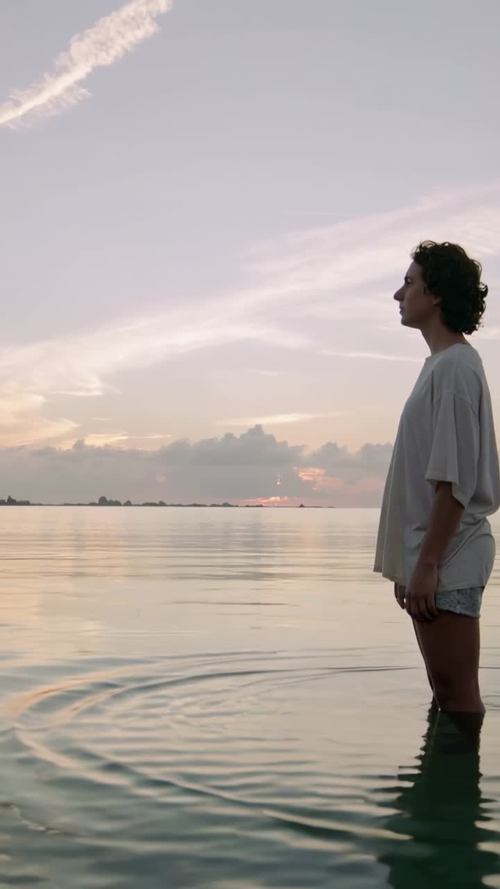 Video verticale: Uomo in piedi che crea increspature dopo un calcio in una baia al tramonto, in maglietta e pantaloncini, con spazio per il testo