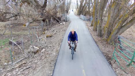 mature, senior man cycling along a path between trees in the countryside - aerial view