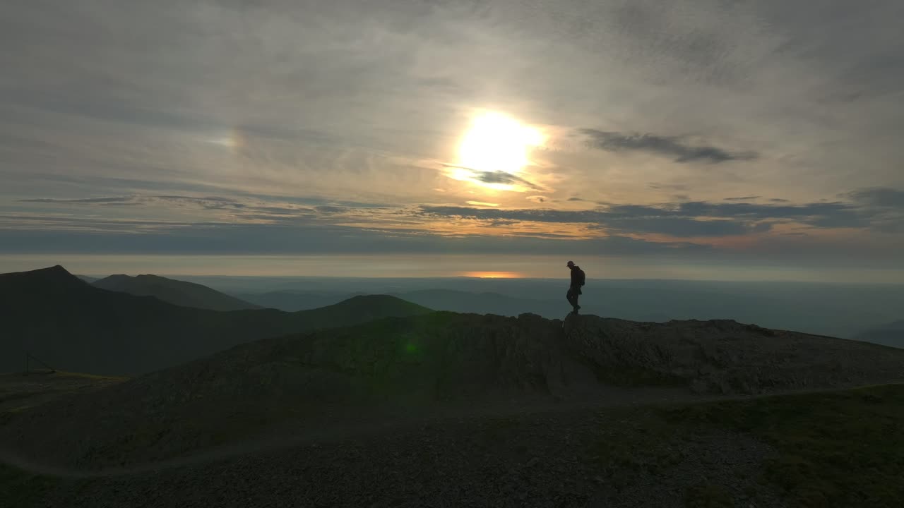 caminante de montaña acercándose a la cumbre siluetada por el sol de la hora de oro