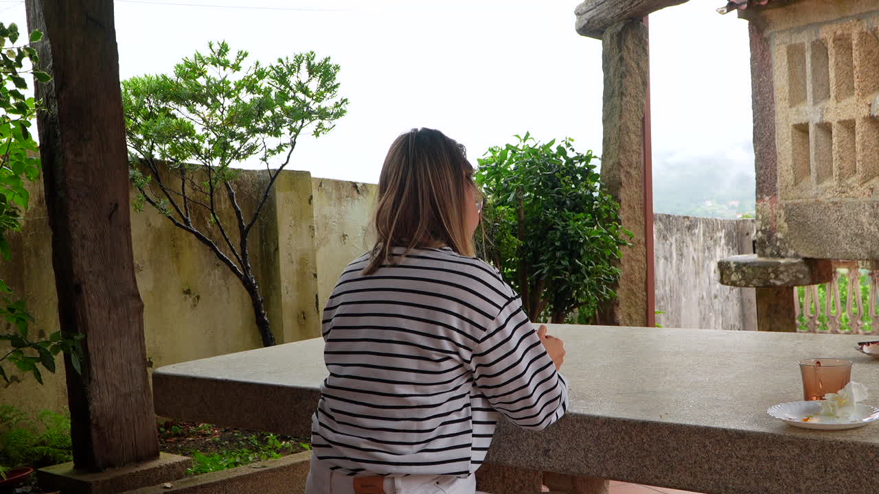 Woman sitting at a stone table outdoors with a misty view