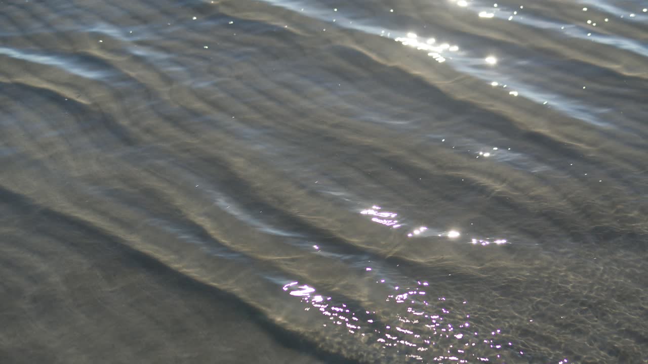 Closeup of gentle water ripples glistening under bright sunlight on sandy beach during warm summer day in Europe showing peaceful motion of waves and calm natural beauty Outdoors