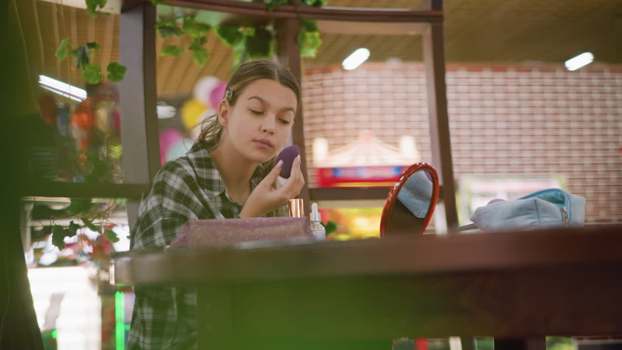 거울을 바라보면서 조용히 메이크업하는 소녀, 나무 테이블에 화장품으로 둘러싸여, 배경에 흐릿한 녹색 잎은 진정하고 자연스러운 환경을 만니다.
