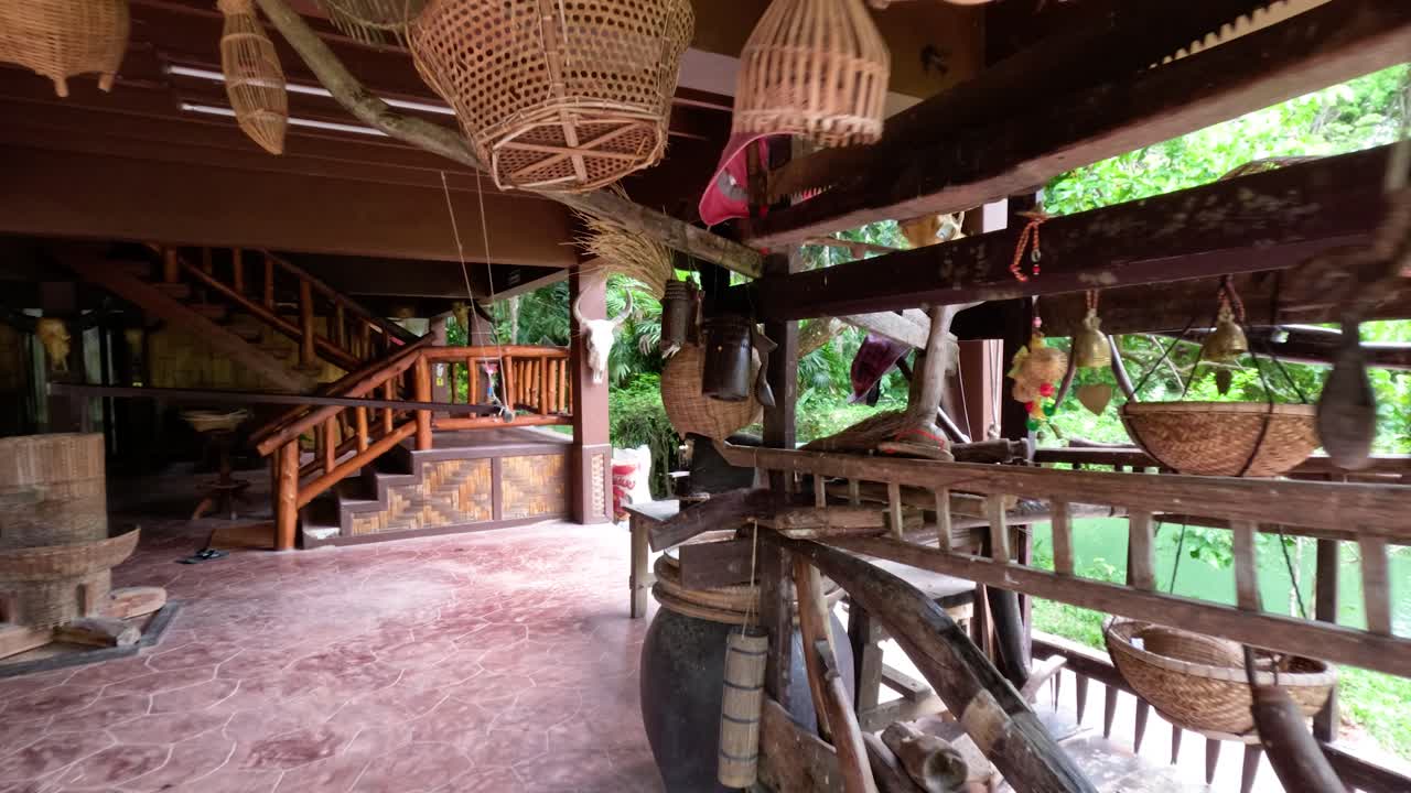 Kamera bergerak melewati alat-alat pertanian tradisional dan keranjang di rumah kayu terbuka, dengan pencahayaan alami
