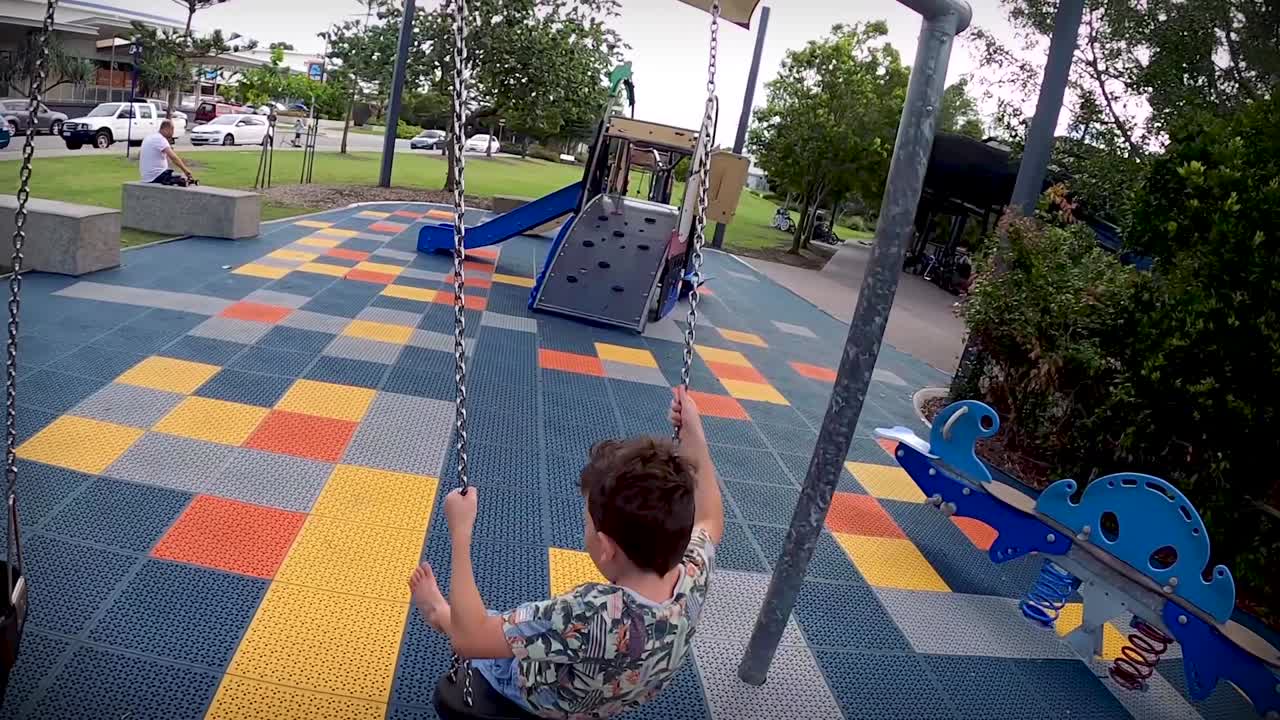 Behind a young boy on a chain swing at a junior playground