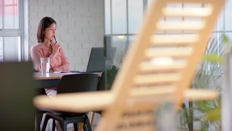 Happy-asian-businesswoman-using-laptop-and-making-notes,-at-table-in-meeting-room,-in-slow-motion