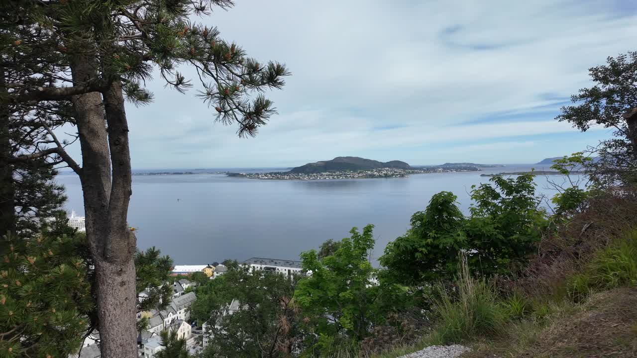 Pemandangan panorama Alesund, Norwegia yang menakjubkan, menampilkan perairan fjord yang tenang, pulau di kejauhan, pepohonan hijau rimbun, dan langit mendung. Sempurna untuk konten perjalanan dan alam