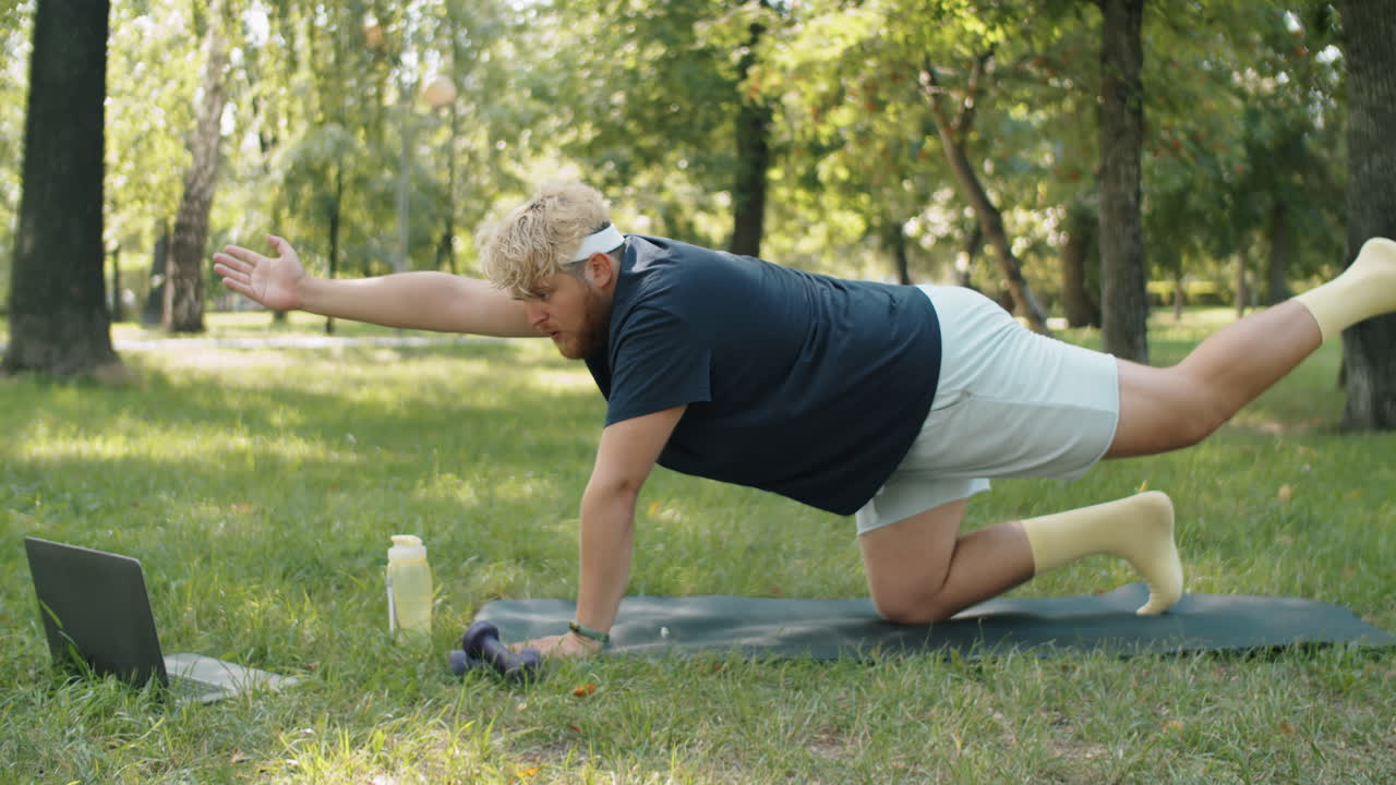 hombre con sobrepeso viendo entrenamiento en línea en una computadora portátil y practicando yoga en el parque