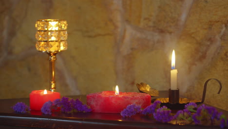 toma panorámica de un ambiente relajante iluminado por velas y candelabros con flores púrpuras, pared de piedra natural y una agradable profundidad de campo poco profunda