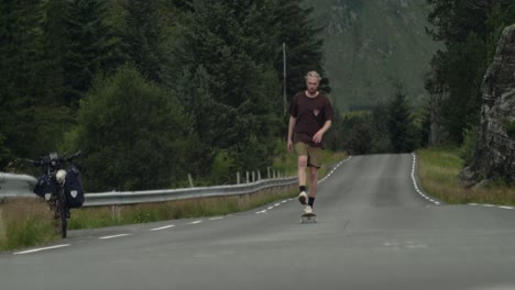 Joven-Patinador-Caucásico-Patinando-Cuesta-Arriba-Hacia-La-Cámara-En-Una-Carretera-Desolada-En-Medio-De-La-Nada-En-Noruega,-Escandinavia