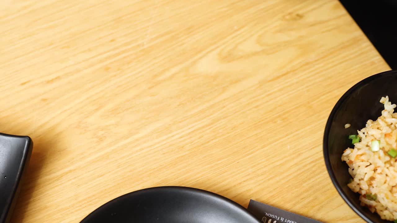 Overhead shot of hand grabbing salmon sushi hand roll under bright restaurant lighting