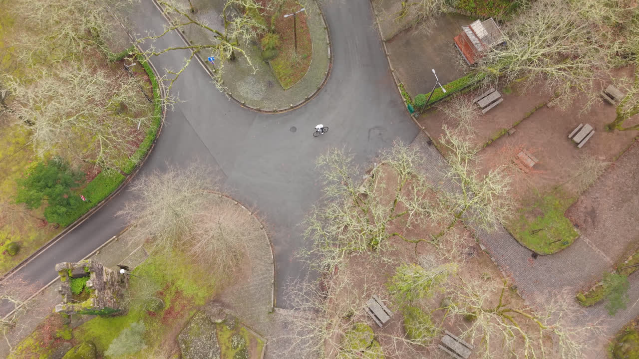 Drone crane down movement tracking cyclist on winding park roadway