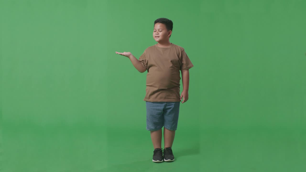 녹색 스크린에 서 있는 동안 을 가리키는 미소와 함께 아시아 소년의 전체 몸
