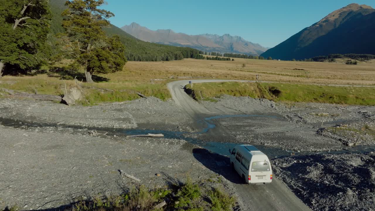 Aerial drone view of white tourist campervan splashing through shallow river crossing in Dart Valley, Glenorchy, South Island of New Zealand Aotearoa