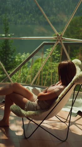 lady sits in armchair and looks at boat sailing along river. woman relieves stress in peaceful natural environment. great landscape of lake with crystal water