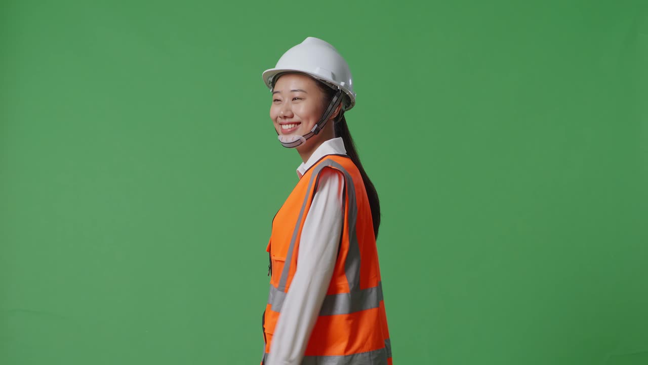 안전 헬을 입은 아시아 여성 엔지니어가 녹색 스크린 배경 스튜디오에서 는 동안 주위를 둘러보고 있는 측면 시각