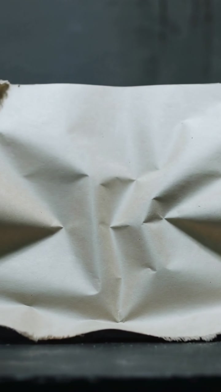Vertical video: Off-frame force pushing white sheet, creasing and tearing at ledge and backing