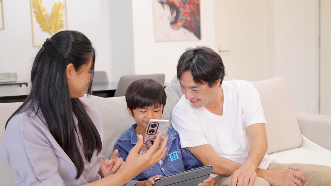 Parents and child interact with digital devices on sofa, bright home, cheerful mood, natural lighting