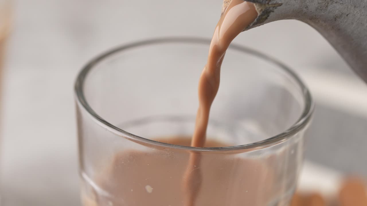 Chai indiano servito in tazze di vetro, preparato in un bollitore di metallo con masalas aromatici. Viene versato nel vetro.