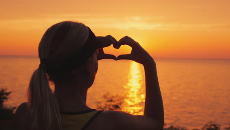 una mujer mira el mar donde se pone el sol muestra una figura en forma de corazón