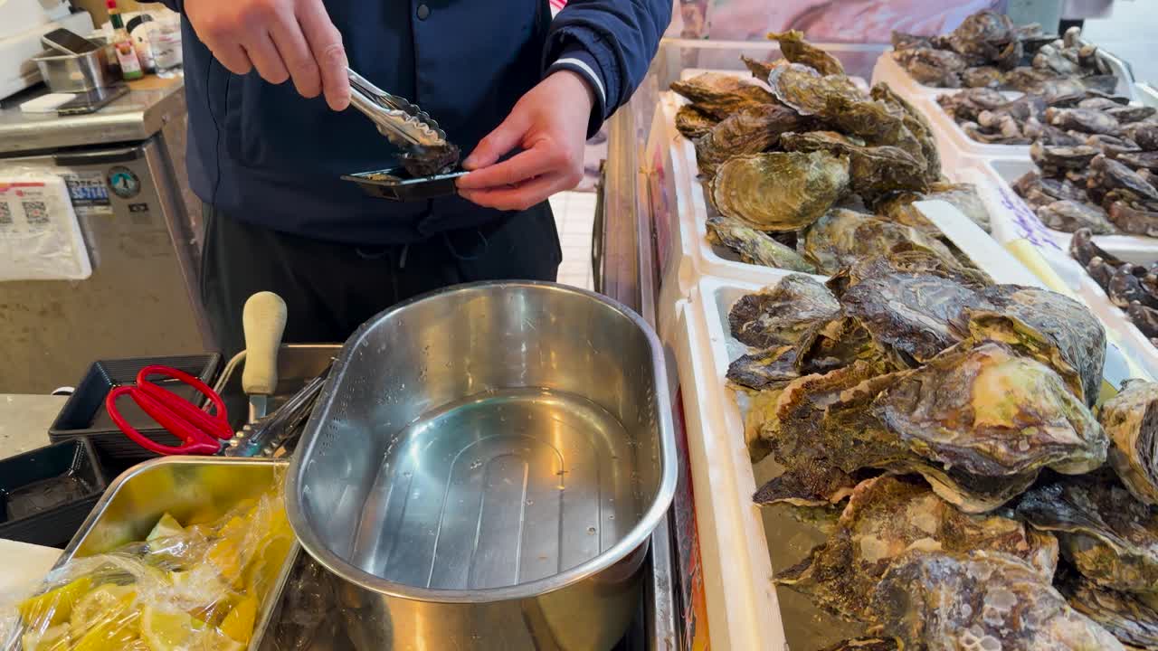A vendor uses tongs to select and prepare fresh oysters for customers in Tokyo