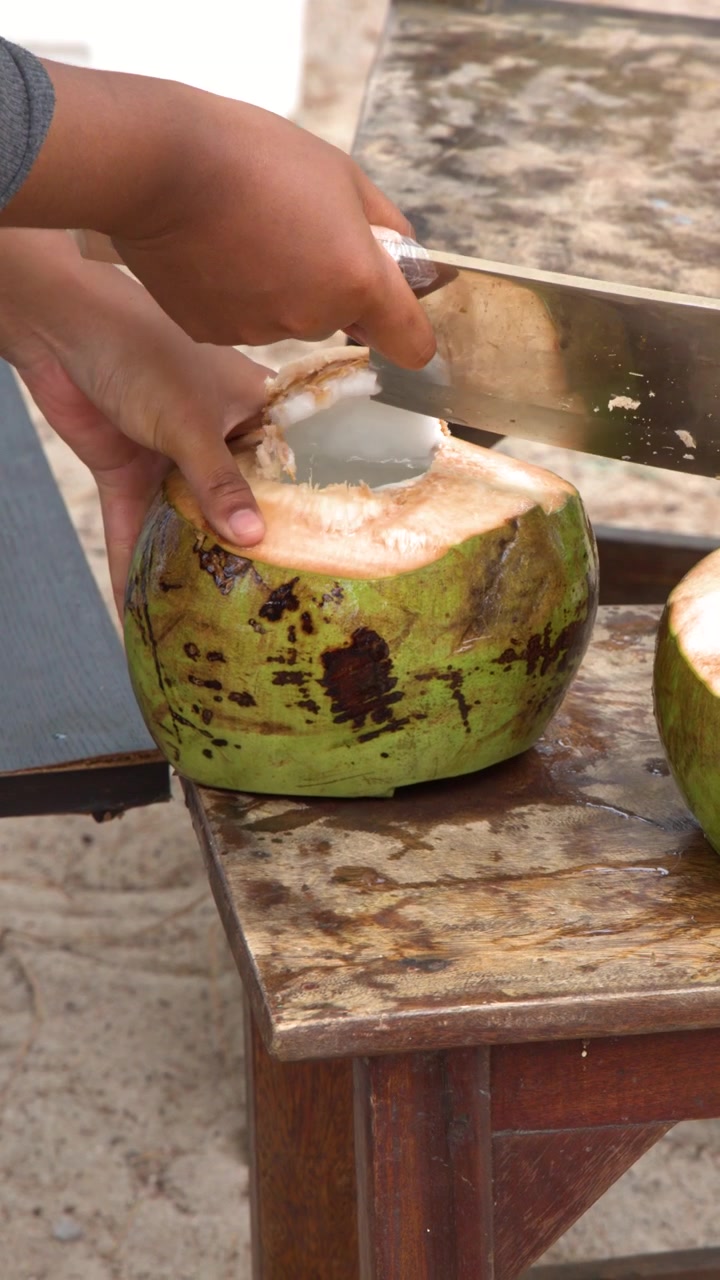Close-up of Hands Opening a Fresh Green Coconut with a Knife