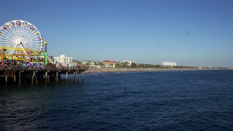 panning left view santa monica pier ferris wheel and roller coaster with a view of the pacific ocean and the beach in the background