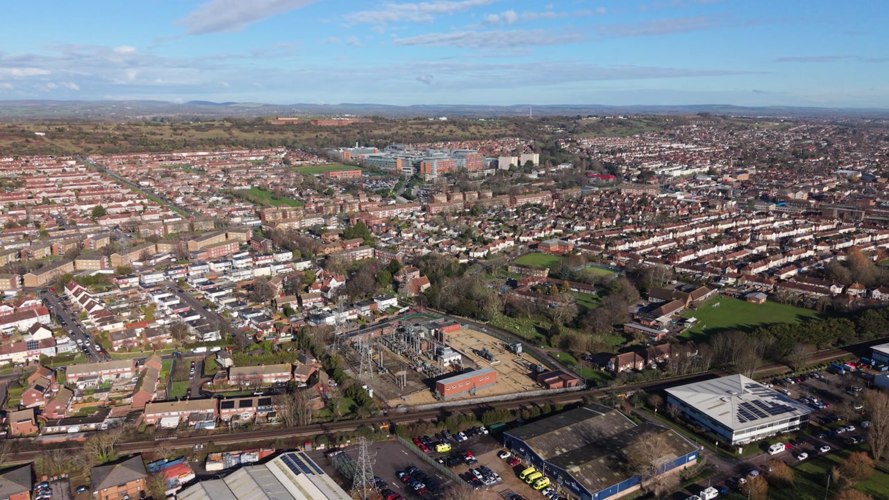 Portsmouth slow high drone flight over mixed urban area towards Queen Alexandra Hospital with distant countryside views on bright sunny day