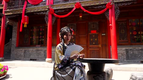 Chinese-woman-dressed-up-like-a-Qing-empress-uses-hand-fan-on-sunny-day-looking-at-camera