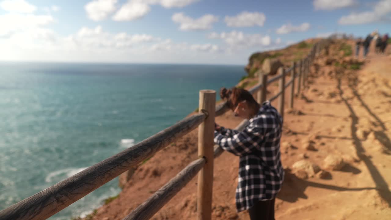 mujer tomando una foto junto al acantilado del océano