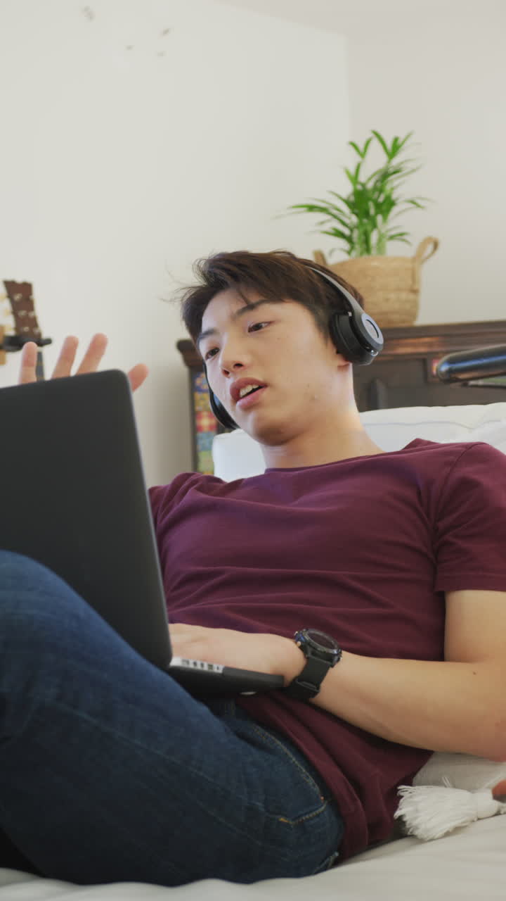 아시안 남성 십대가 거실에서 노트북을 사용하는 수직 비디오