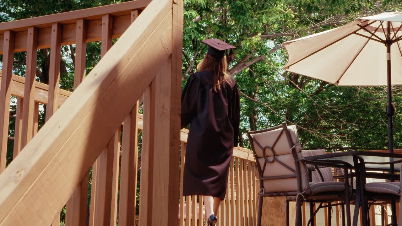 A female graduate student walks to edge of wooden balcony holding diploma.