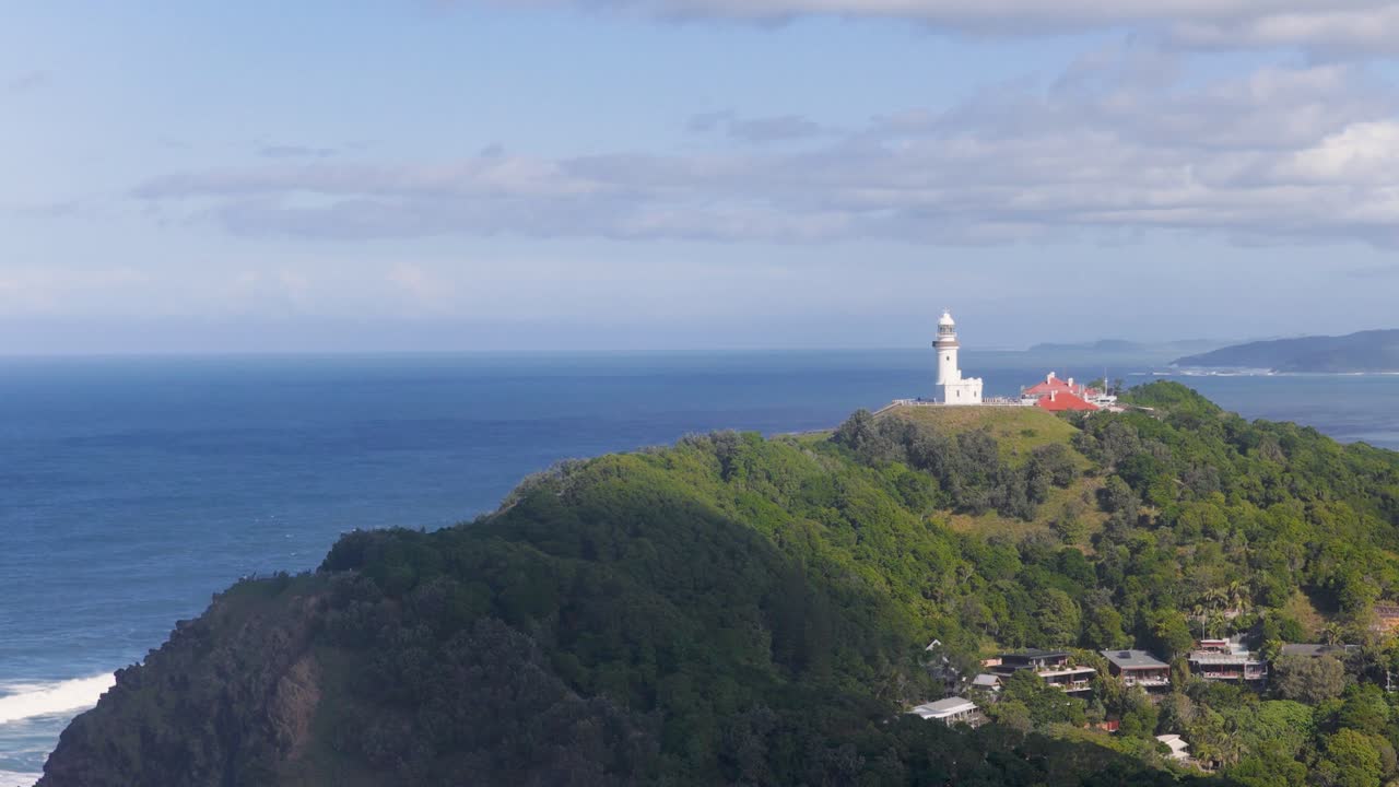 Drone footage captures Byron Bay lighthouse atop lush cliffs with expansive ocean views under clear skies