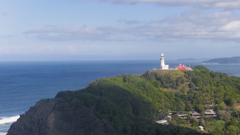 drone footage captures byron bay lighthouse atop lush cliffs with expansive ocean views under clear skies