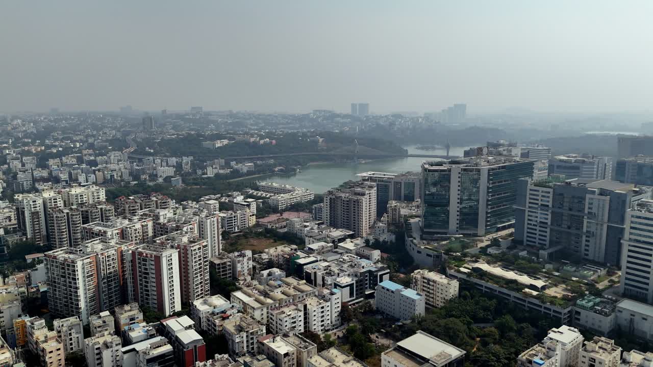Durgam Cheruvu scintilla accanto allo skyline tecnologico di Hyderabad, un lago urbano incorniciato da torri di vetro, fitti insediamenti abitativi e la caratteristica foschia della città.