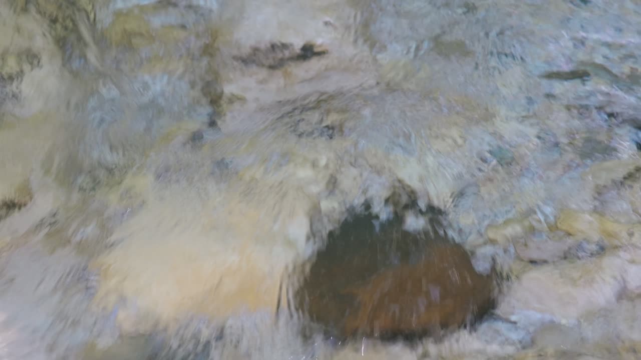 Static shot of clear, transparent water rushing over a bed of stones.