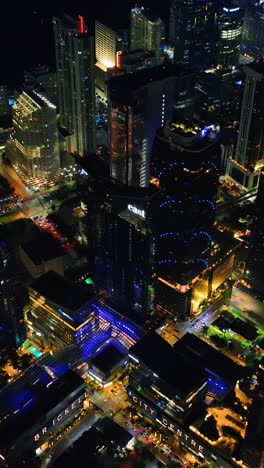 flying closer to the tops of skyscrapers in the downtown of miami, florida. stunning view of usa city at night. vertical video