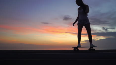 beautiful girl rides a skateboard on the road against the sunset sky