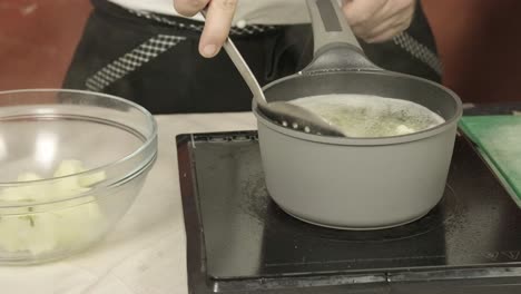 chef uses skimmer to remove cauliflower florets after blanching in hot water to soften