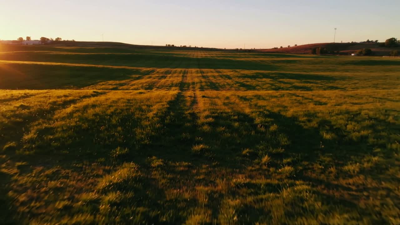 Drone in volo che riprende un campo erboso centrale con tracce parallele all'ora d'oro, ombra triangolare.