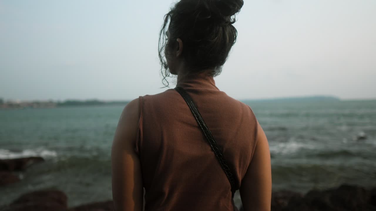 A woman standing by the sea looks out at the horizon during the day