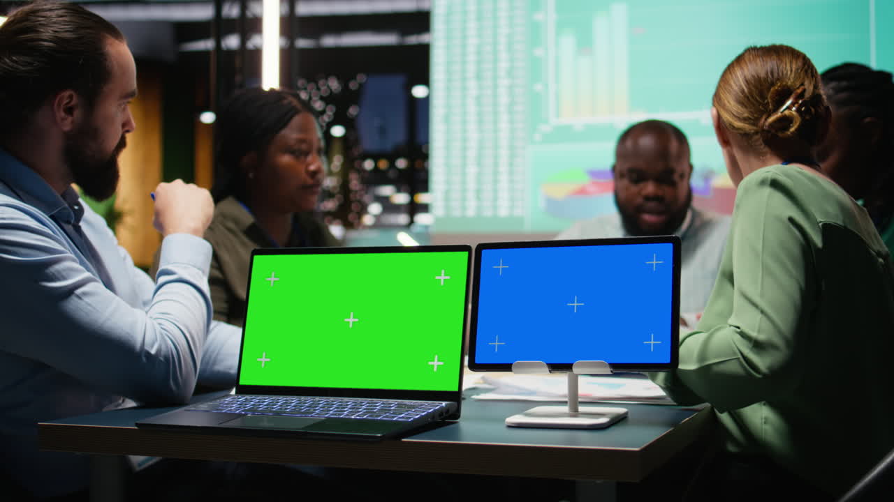 Company associates briefing after hours next to chroma key screen