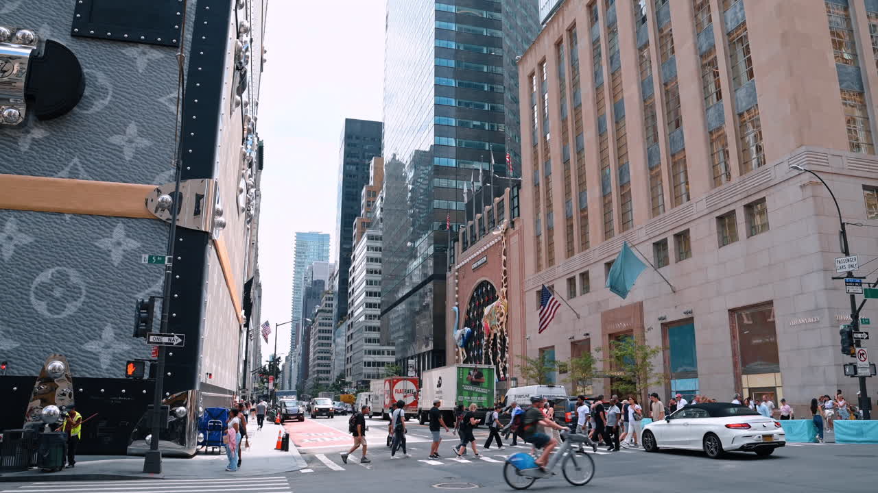 New York, USA, 1 agosto 2025: Incrocio affollato sulla Fifth Avenue con negozi e grattacieli. Persone e auto riempiono un trafficato incrocio lungo la Fifth Avenue
