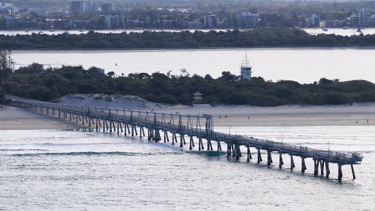 Ampia inquadratura dall'alto del pontile industriale per il bypass della sabbia che si estende nelle onde dell'oceano.