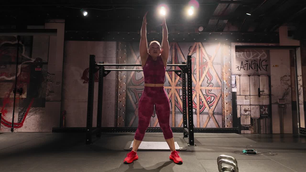 Vista frontale di una donna forte che esegue thruster con manubri. Un esercizio composto per tutto il corpo che combina uno squat e una pressa sopra la testa per un allenamento potente.