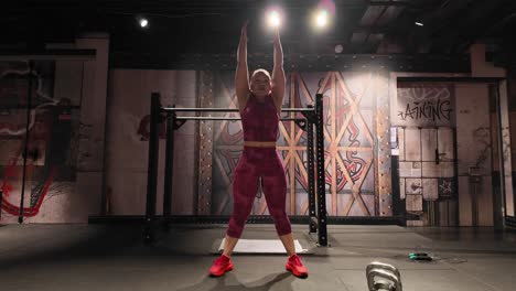 front view of a strong woman performing dumbbell thrusters. a full-body compound exercise combining a squat and an overhead press for a powerful workout