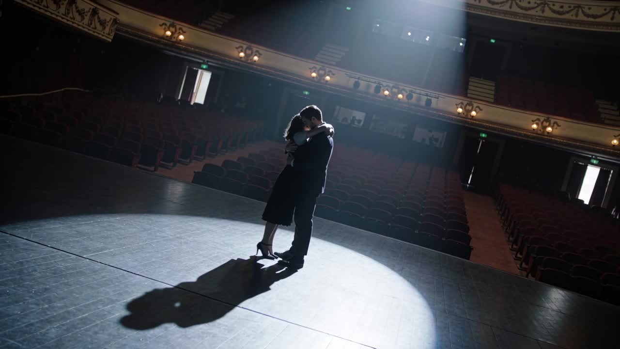 Spotlight turning on, man in suit and woman in dress holding embrace on ornate stage, rehearsing