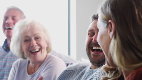 senior parents with adult offspring sitting on sofa at home talking and laughing